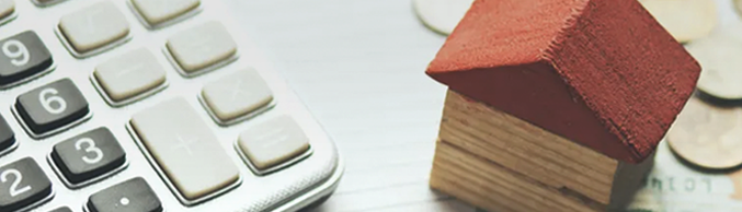 Close-up of calculator and coins next to a miniature wooden house with red roof